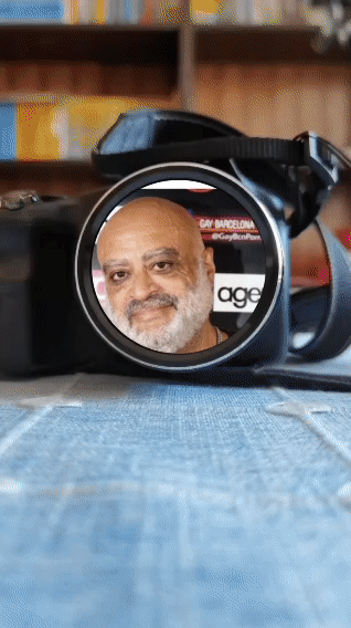 lv_0_20250617191051 GIF animado de una cámara fotográfica enfocando un retrato de Oswaldo Martín, director de cine y fotógrafo. El objetivo de la cámara refleja su rostro con claridad, sobre un fondo desenfocado de libros y estantería.