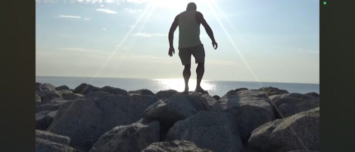Figura humana camina sobre rocas al atardecer en blanco y negro