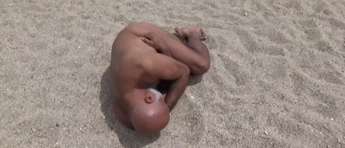 Cuerpo desnudo en posición fetal sobre la arena